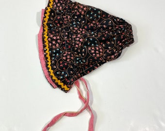 May include: A black bonnet with a floral print and yellow and pink trim. The bonnet has a long pink ribbon tie.