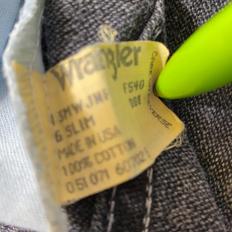 Może przedstawiać: Ż&oacute;łta metka dżins&oacute;w Wrangler z tekstem "13MW JMF F540 008 6 SLIM MADE IN USA 100% COTTON 051071 607025" i "CARE ON REVERSE".