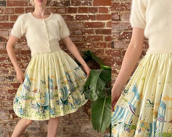 May include: A yellow and white skirt with a whimsical print of a carnival scene. The skirt is full and has a gathered waist. A white cardigan is worn over the skirt.