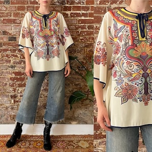 May include: A white, long-sleeved,  boho-style top with a colorful floral and bird print. The top has a wide, flowing silhouette and a navy blue trim.