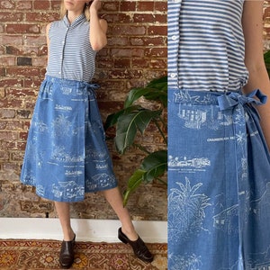 May include: A blue denim wrap skirt with a white print of houses and palm trees. The skirt has a tie closure at the waist and is knee-length.