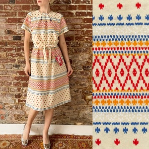 May include: A white dress with a red, blue, and yellow geometric pattern. The dress has a tie at the waist and a red tag that says "Size 12".
