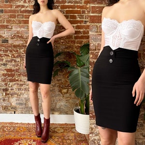 May include: A black pencil skirt with a high waist and two silver buttons. The skirt is paired with a white lace bustier top.
