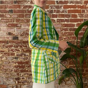 May include: A green, yellow and blue plaid blazer. The blazer has a double-breasted closure and a single pocket on the right side.