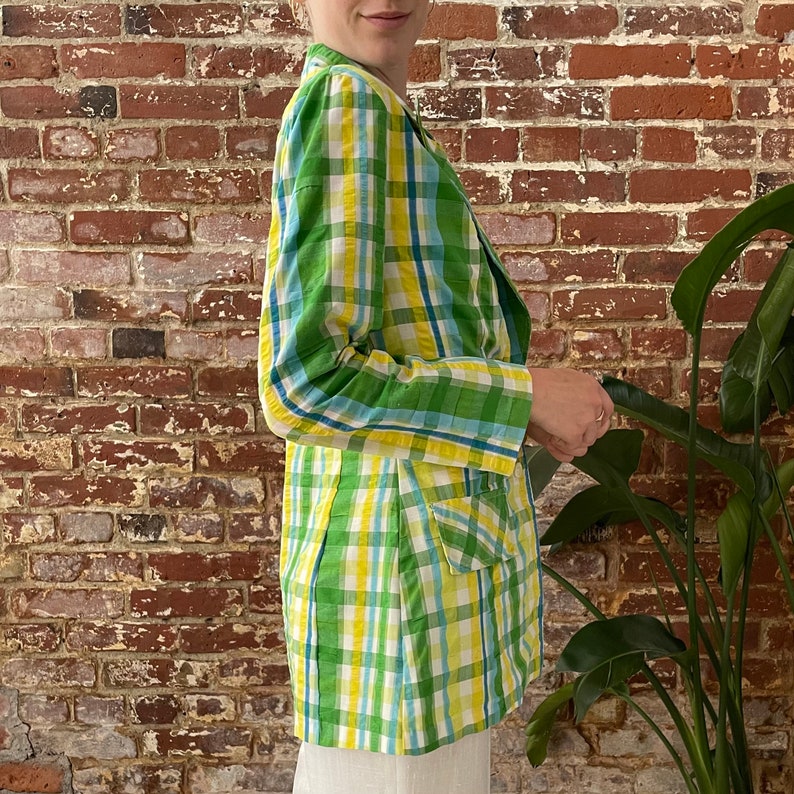 May include: A green, yellow and blue plaid blazer. The blazer has a double-breasted closure and a single pocket on the right side.
