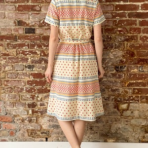 May include: A white midi dress with a geometric pattern in red, blue, and yellow. The dress has a short sleeve and a fitted bodice.