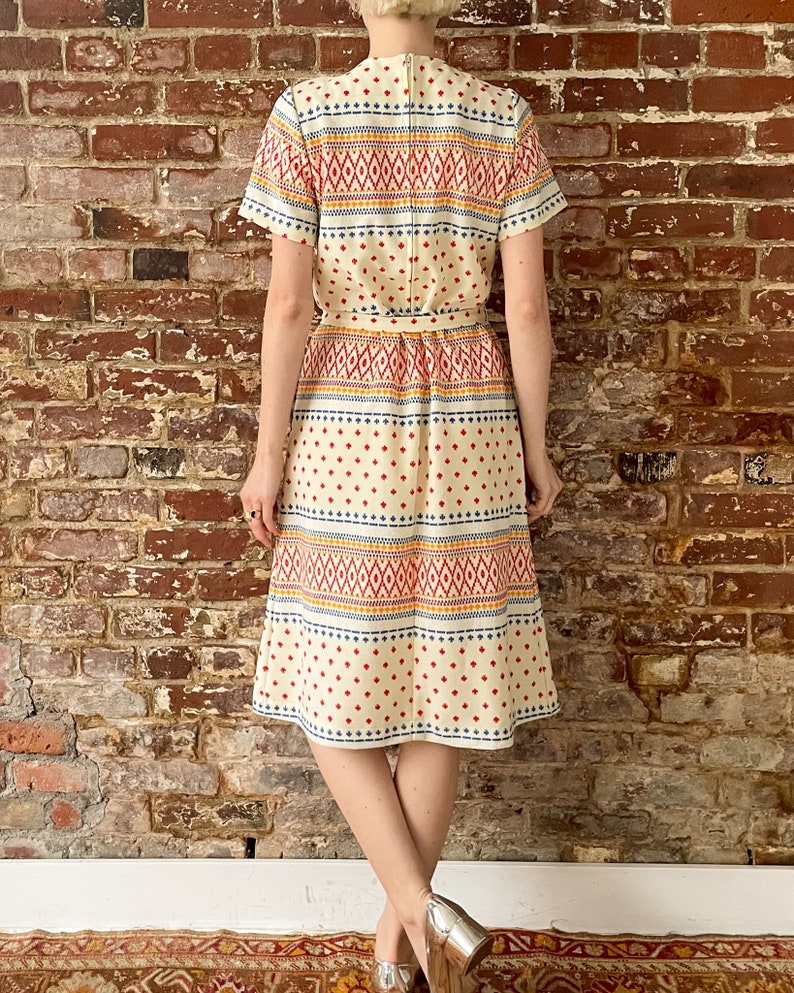 May include: A white midi dress with a geometric pattern in red, blue, and yellow. The dress has a short sleeve and a fitted bodice.