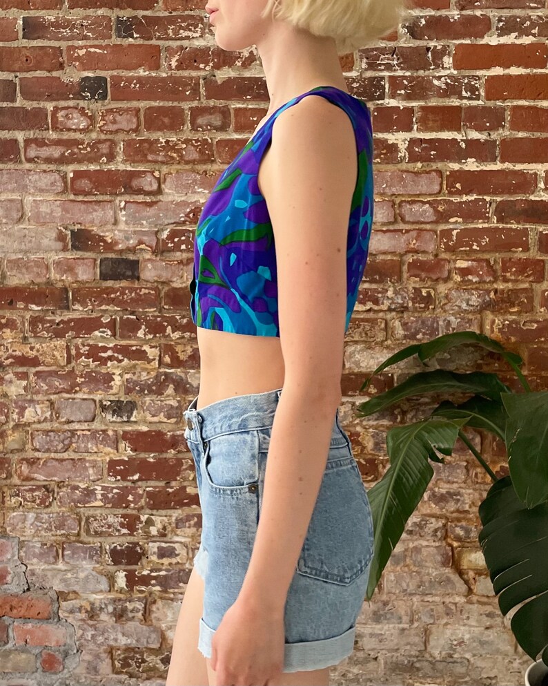 Peut inclure: Un haut court sans manches bleu et vert avec un motif floral. Le haut est port&eacute; avec un short en jean bleu clair.