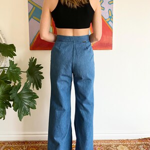 Puede incluir: Un top corto negro combinado con unos vaqueros de mezclilla azul de cintura alta y acampanados. Los vaqueros tienen un dise&ntilde;o cl&aacute;sico de cinco bolsillos y una pernera ancha. El conjunto tiene un estilo vintage, adecuado para ropa informal.