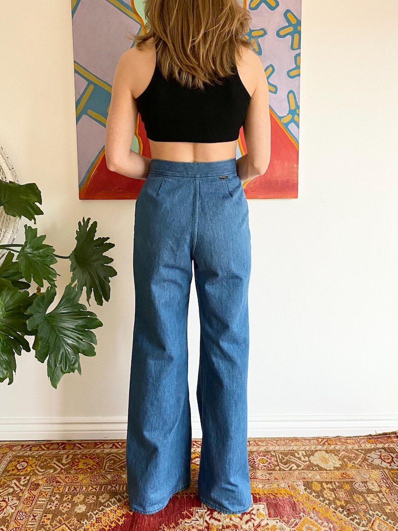 Puede incluir: Un top corto negro combinado con unos vaqueros de mezclilla azul de cintura alta y acampanados. Los vaqueros tienen un dise&ntilde;o cl&aacute;sico de cinco bolsillos y una pernera ancha. El conjunto tiene un estilo vintage, adecuado para ropa informal.