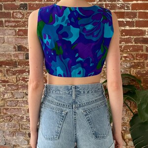 Peut inclure: Un haut court sans manches avec un imprim&eacute; floral abstrait bleu, vert et violet. Le haut est fait d'un tissu l&eacute;ger et a une coupe d&eacute;contract&eacute;e.