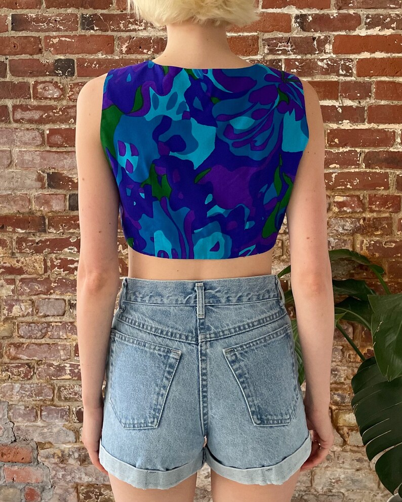 Peut inclure: Un haut court sans manches avec un imprim&eacute; floral abstrait bleu, vert et violet. Le haut est fait d'un tissu l&eacute;ger et a une coupe d&eacute;contract&eacute;e.