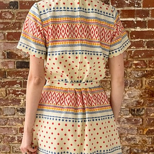 May include: A white dress with a geometric pattern in red, blue, and yellow. The dress has a short sleeve and a fitted bodice. The skirt is full and flows to the knees.