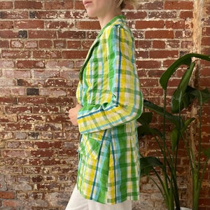 May include: A green, yellow and blue plaid blazer with a long, fitted silhouette. The blazer has a single button closure and two pockets.