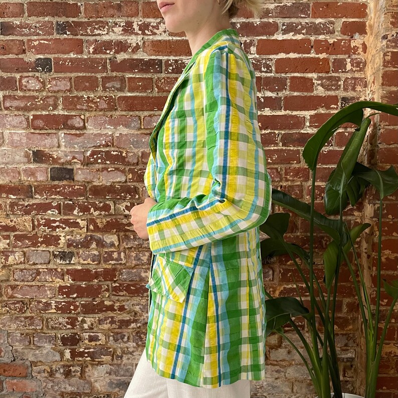 May include: A green, yellow and blue plaid blazer with a long, fitted silhouette. The blazer has a single button closure and two pockets.