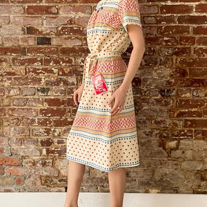 May include: A cream-colored dress with a geometric pattern in red, blue, and yellow. The dress has a short sleeve and a tie belt. The dress has a tag that says "Royal" in red letters.