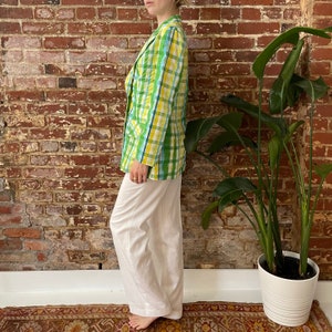 May include: A green and yellow plaid blazer with a white background. The blazer is worn with white trousers.