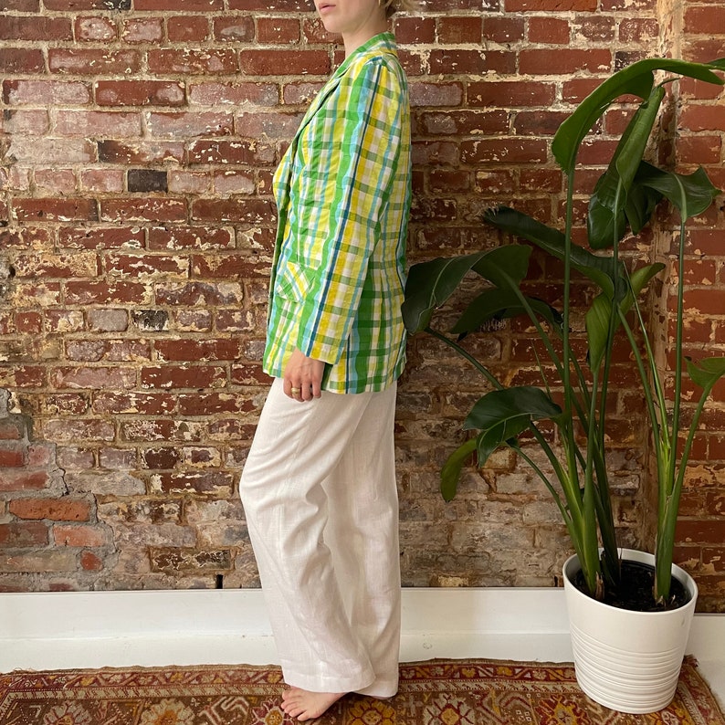 May include: A green and yellow plaid blazer with a white background. The blazer is worn with white trousers.