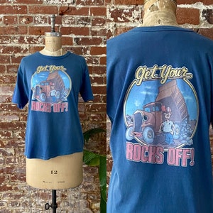 May include: A blue t-shirt featuring a graphic on the front and back. The front graphic says "Get Your Rocks Off!" with a cartoon truck and person. The back graphic is similar.