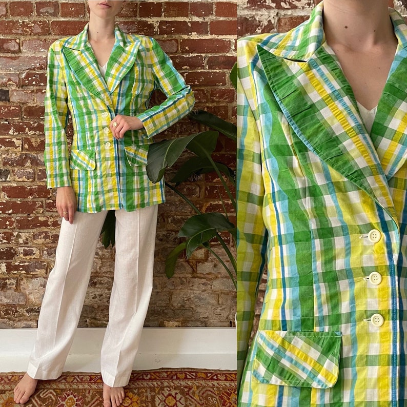May include: A green, yellow and blue plaid blazer with a ruffled collar and two pockets. The blazer has a double-breasted closure with three buttons.