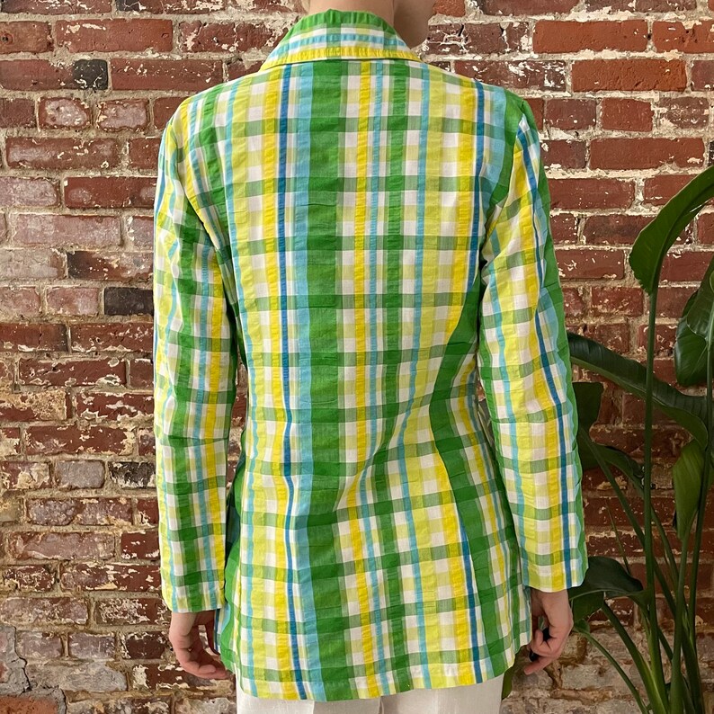 May include: A green, yellow and blue plaid blazer. The blazer has a long sleeve and a collar.
