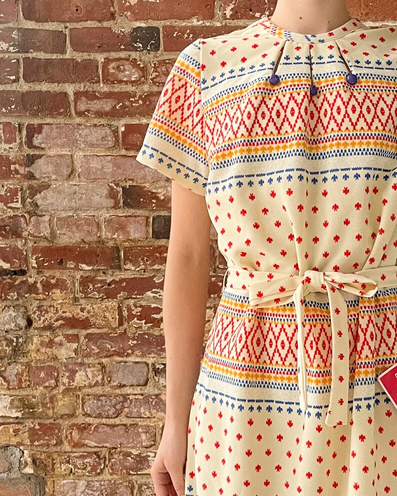 May include: A white dress with a geometric pattern in red, blue, and yellow. The dress has a short sleeve and a tie belt.