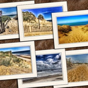 May include: A collection of framed photographs featuring beach scenes. Each photo showcases sandy paths, dunes, and the ocean under blue skies. Some images include wooden fences and signs, capturing the natural beauty of the coast.
