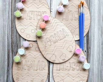 May include: Five wooden Easter egg shaped paint-by-number kits with names "Easton", "Rosalia", "Skylar", "Lawson", and "Ansley" written on them. Each kit includes paint pots and paintbrushes.