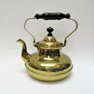 May include: A brass teapot with a black wooden handle. The teapot has a round body and a spout on the side. The teapot is polished and shiny.