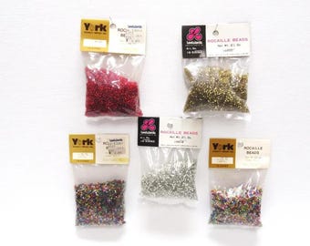 May include: Five sealed bags of rocaille beads in various colors, including red, gold, silver, and multicolored. Each bag has a paper label with the brand name "York" or "Leedwards" and product information.