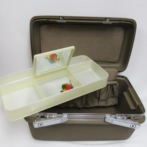 May include: Open brown vintage jewelry box with a cream-colored tray and mirror. The tray has three compartments and a small mirror. The box is open, revealing a brown interior with a small pouch. Two colorful pins are visible.
