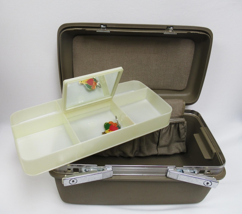 May include: Open brown vintage jewelry box with a cream-colored tray and mirror. The tray has three compartments and a small mirror. The box is open, revealing a brown interior with a small pouch. Two colorful pins are visible.