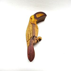 May include: A wooden toucan bird puzzle box with a brown, yellow, and red finish. The toucan's beak is open and the box is closed.