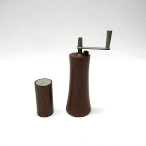 May include: A wooden salt and pepper grinder set with a silver crank. The grinder is brown and has a cylindrical shape.