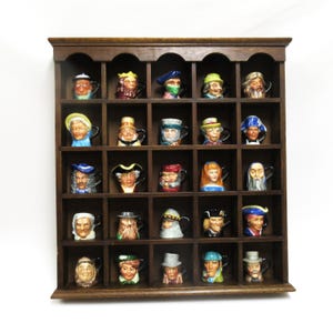 May include: A dark wooden display shelf filled with miniature ceramic mugs, each featuring a different historical figure's face. The mugs are brightly colored and arranged in a grid pattern, creating a unique collection.