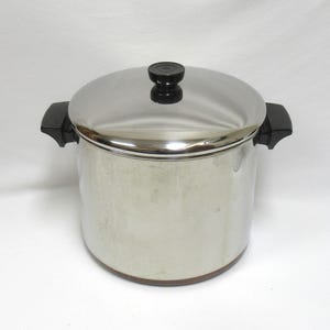 May include: A stainless steel cooking pot with a lid and black handles. The pot has a shiny, reflective surface and a dark knob on the lid. The pot is designed for cooking and food preparation.