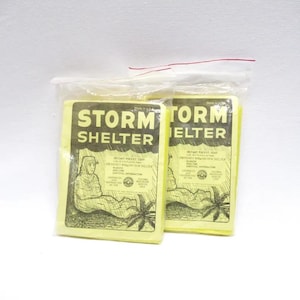 May include: Two yellow packages containing Storm Shelter Instant Pocket Tents. The packages have black text and illustrations of a person using the tent. The text on the package reads "Storm Shelter Instant Pocket Tent Emergency Blanket Rain Shelter".