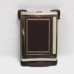 May include: A vintage address book with a dark brown cover and a gold-colored border. The book has a silver-colored frame and a lettered index on the side. The base and side pieces are a dark brown color.