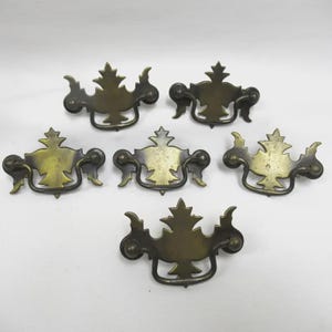 May include: Six antique brass drawer pulls with a leaf design. Each pull features a central leaf shape with curved handles and decorative accents. The brass has a warm, aged patina, suggesting vintage or retro style.