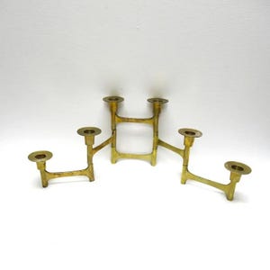 May include: A vintage brass candelabra with five candle holders. The candelabra has a geometric design with a central rectangular base and arms extending outwards. The brass has a warm, aged patina, suggesting it is an antique or vintage piece.