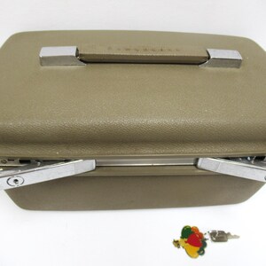 May include: A vintage olive green Samsonite suitcase with a textured surface, chrome accents, and a handle. The suitcase has two chrome latches and a small key with a colorful charm.