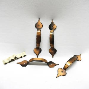 May include: Five antique copper door pulls with a heart-shaped design. The pulls have a dark brown patina and a slightly textured surface.