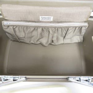 May include: Open view of a vintage Samsonite Saturn suitcase. The interior is a light tan color with a matching fabric pocket and a zippered compartment. The Samsonite Saturn label is visible. The suitcase has metal hinges and clasps.