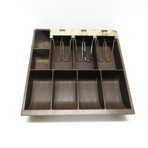 May include: A brown metal cash drawer with six compartments and metal dividers. The drawer has a metal frame with a silver finish.