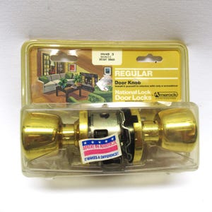 May include: A new, bright brass door knob set in its original packaging. The packaging includes the text "REGULAR Door Knob" and "MADE IN AMERICA". The door knob is a shiny gold color and is ready for installation.