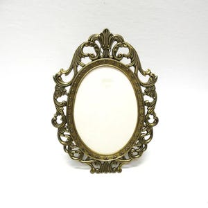 May include: Ornate, antique-style oval picture frame in a bronze finish. The frame features intricate scrollwork and a decorative top and bottom. The center holds an oval space for a photo or artwork.