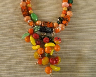 May include: A multi-strand necklace made of orange, yellow, and green glass beads. The necklace has a pendant made of a cluster of smaller beads in the same colors.