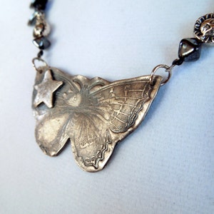 May include: A silver butterfly pendant necklace with a star charm. The necklace is made of metal beads and has a silver chain.