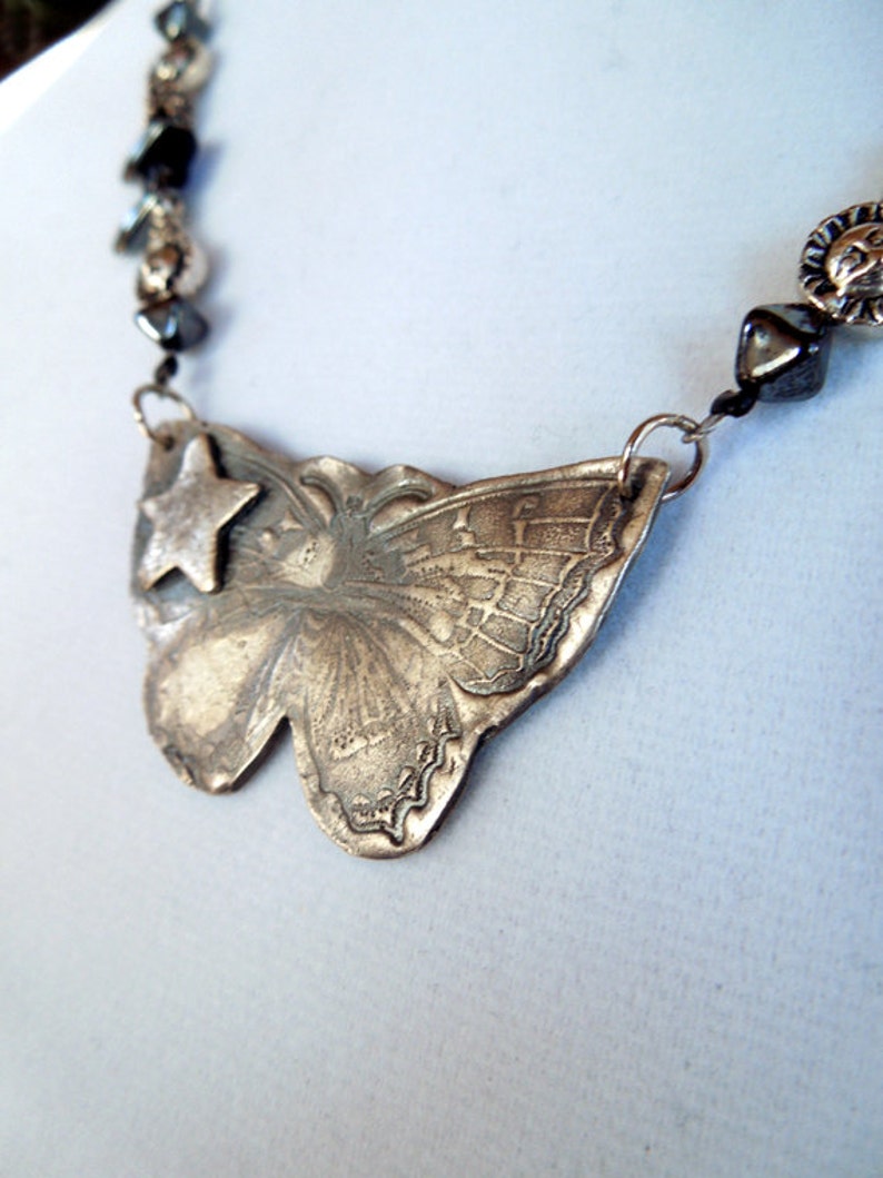 May include: A silver butterfly pendant necklace with a star charm. The necklace is made of metal beads and has a silver chain.