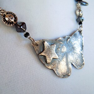 May include: A silver necklace with a butterfly pendant featuring a star design. The necklace is made with silver beads and black beads.